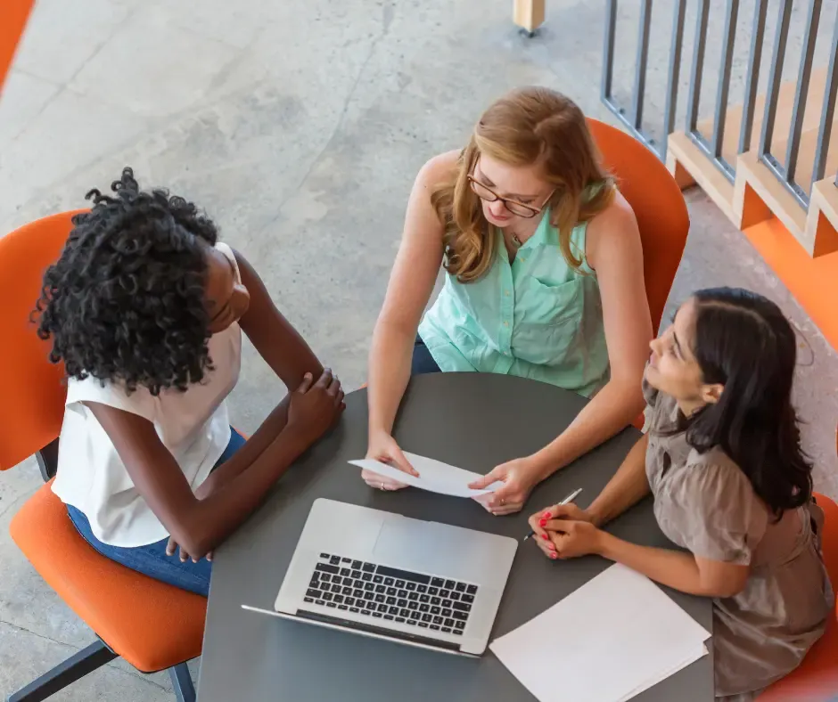Three women collaborating around a laptop